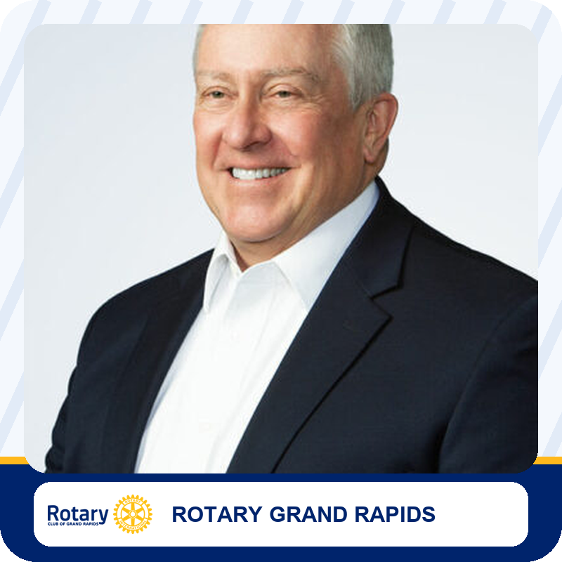 Smiling man in a dark suit and white shirt; portrait used for Rotary Grand Rapids branding.