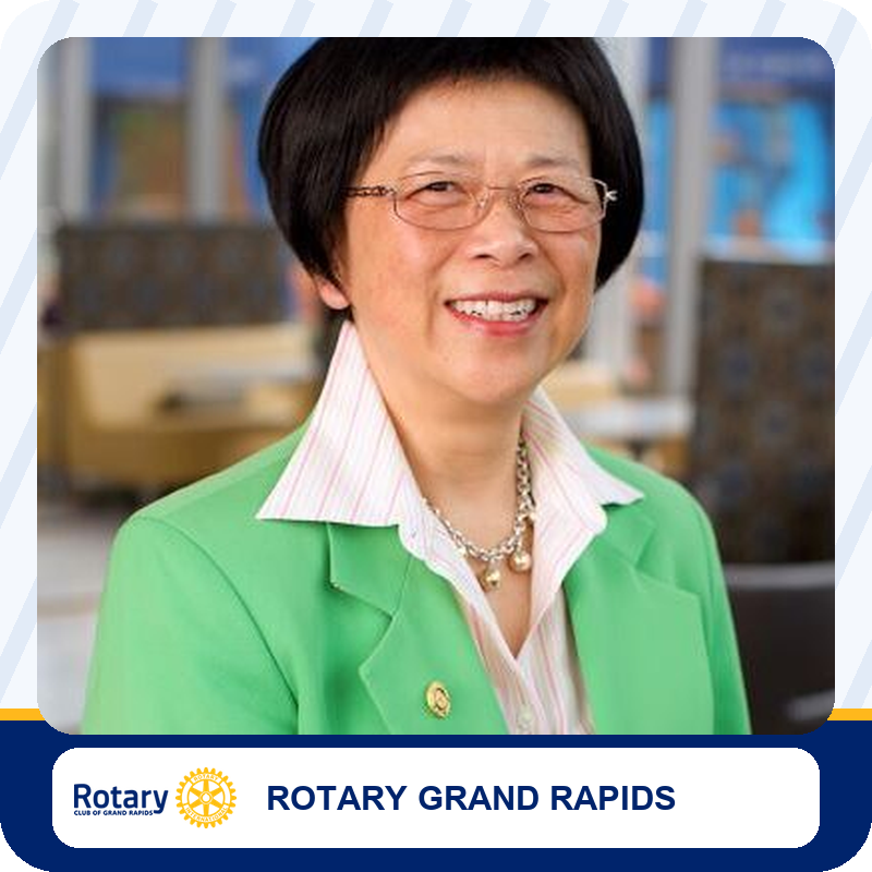 Portrait of a smiling woman wearing a green blazer and striped shirt, in a Rotary Grand Rapids setting.